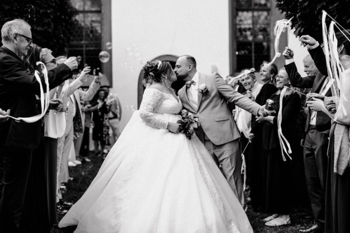 Hochzeitsfotograf Ingelheim Braut und Bräutigam küssten sich umgeben von Gästen, die Konfetti werfen.